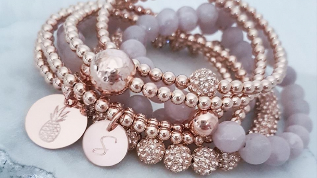 close up shot of rose gold beaded bracelet with a pineapple charm and an S monogram