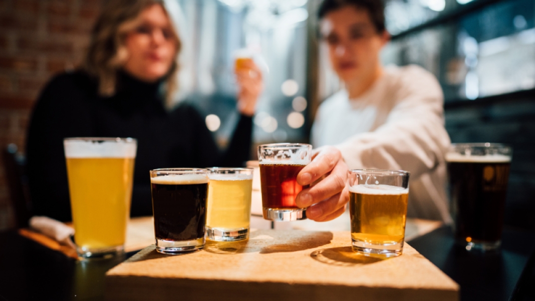 a man and woman with a flight of different coloured beers