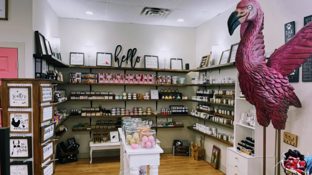 picture of Whimsy store with a right pink flamingo statue in the foreground with its wings stretched and shelves full of product in the background