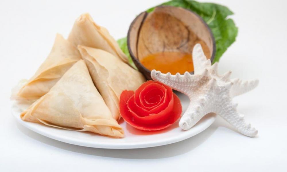 A plate with triangle pastries, a red flower, a white starfish, and half a coconut.