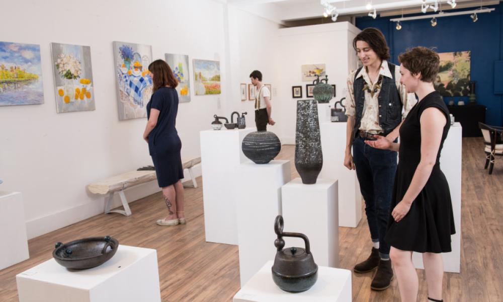 four people in a gallery viewing colourful paintings and black pottery