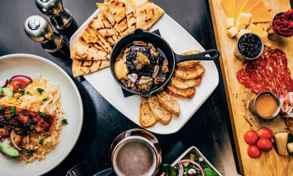 A top down view of a table with various plates of finger foods, including a cheese board and breads with dip.
