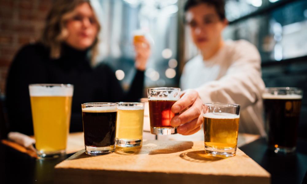 a man and woman with a flight of different coloured beers