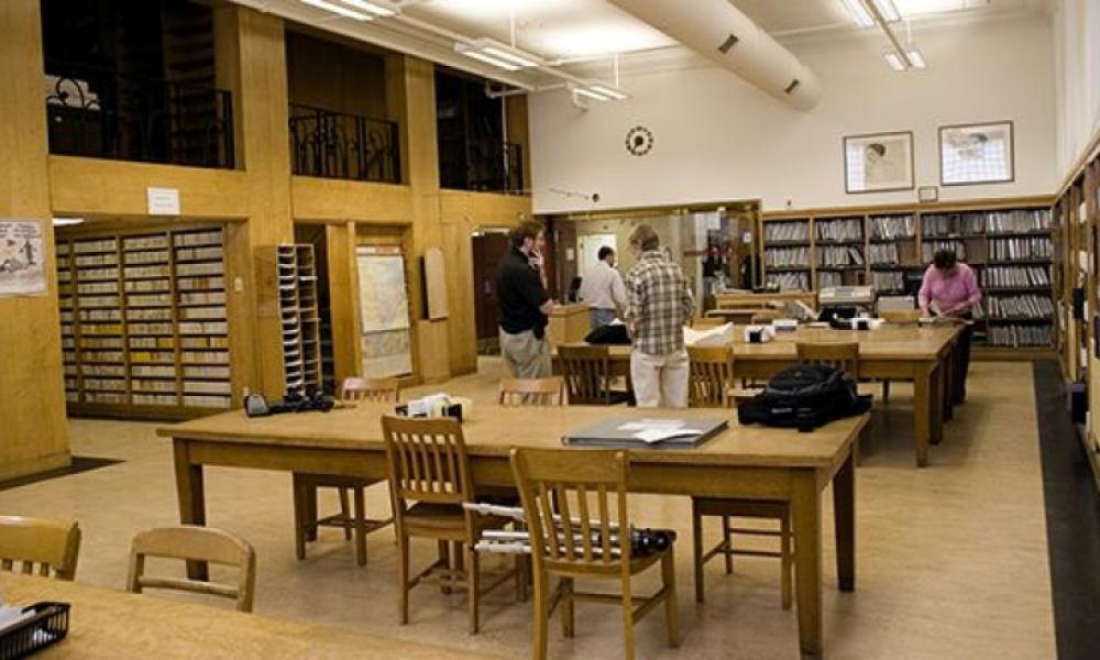 Archival library interior. There are some desks and chairs as well as bookcases filled with archival documents.