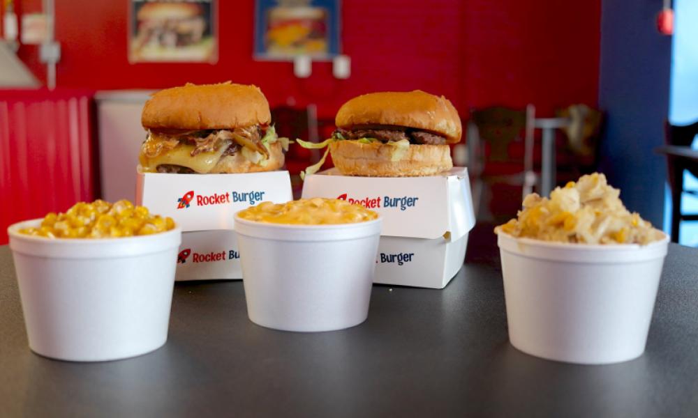 two cheese burgers with three sides in white styrofoam cups