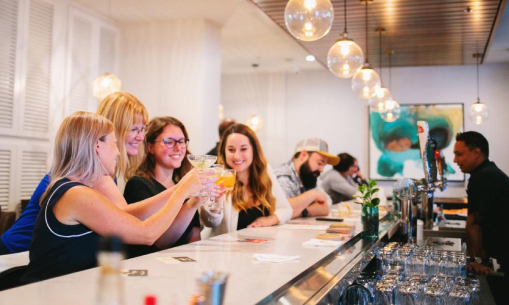 group of women toasting at a white bar with a male bartender