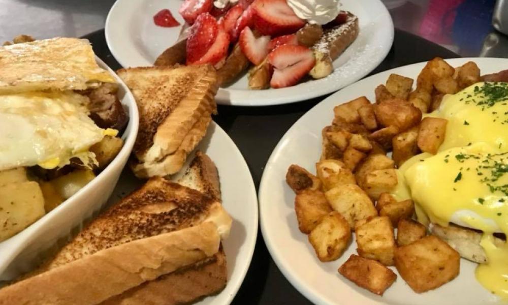 Eggs, toast, hashbrowns, strawberries and other breakfast foods on plates on a table