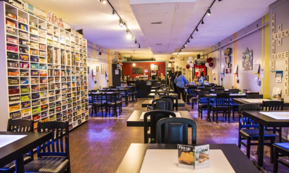 Interior of board game cafe. There a chairs and tables throughout the room and shelving with board games in it